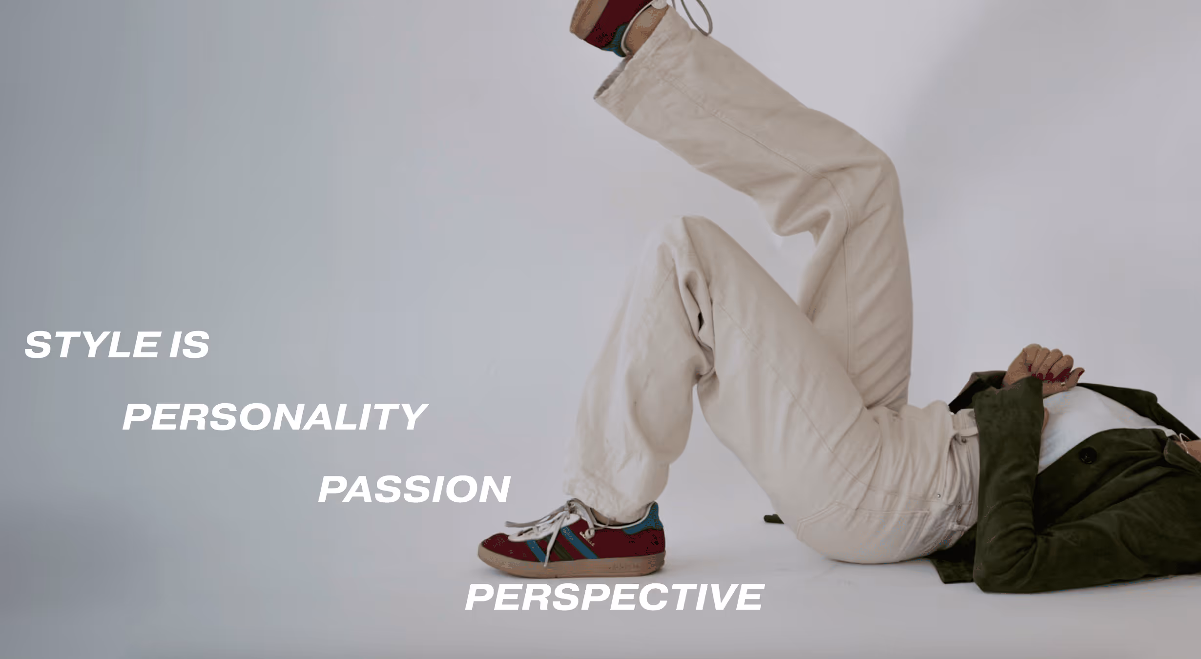 Person lying on back with legs raised, wearing beige pants, dark green jacket, and burgundy sneakers, next to text reading 'STYLE IS PERSONALITY PASSION PERSPECTIVE'.