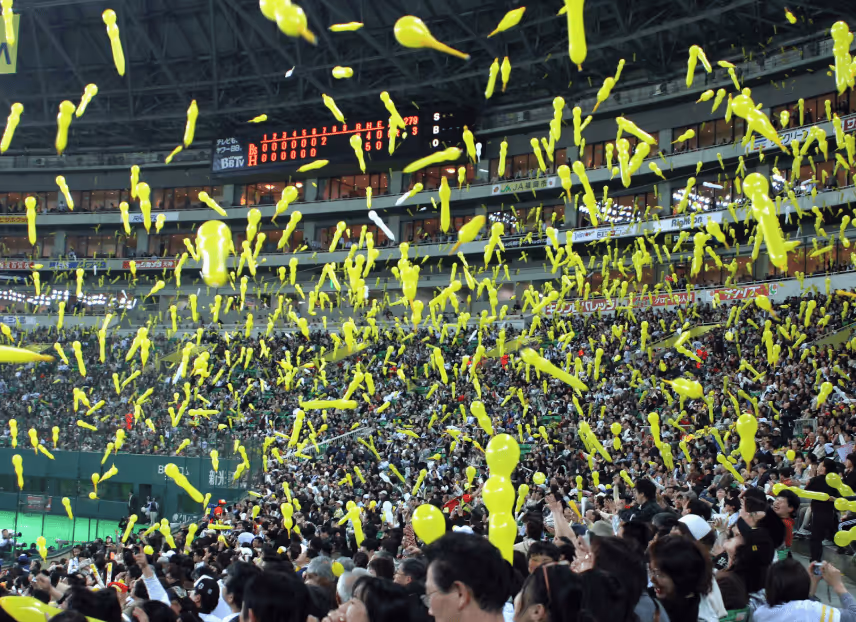 Crowd at a stadium releasing numerous yellow balloons into the air during a baseball game.