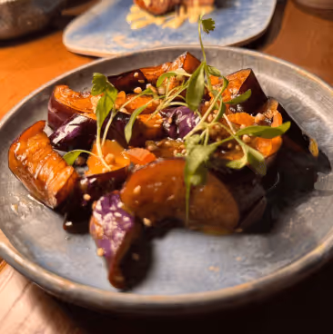 Plate of cooked eggplant garnished with green herbs and sesame seeds on a wooden table.