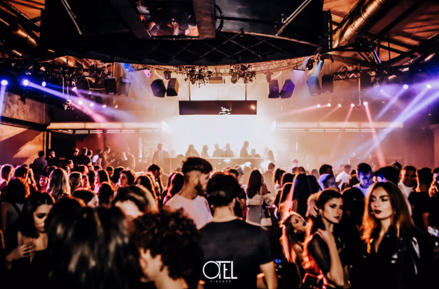 Crowded nightclub with colorful stage lights and people dancing and socializing.