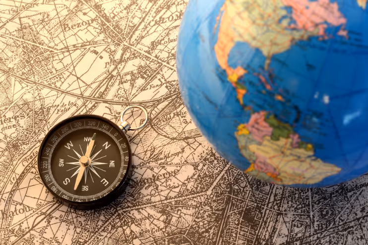 Black compass placed on a vintage map next to a partially visible globe showing the Americas.