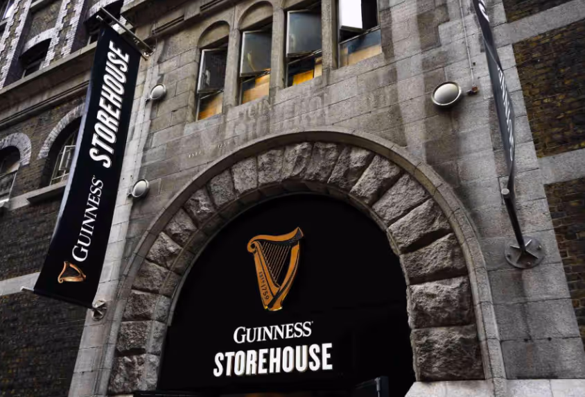 Stone building façade with arched entrance and black signs reading 'Guinness Storehouse' featuring a golden harp logo.