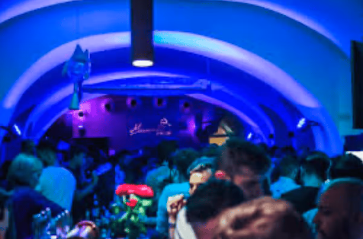 Crowded nightclub interior with blue and purple lighting and people socializing under arched ceilings.