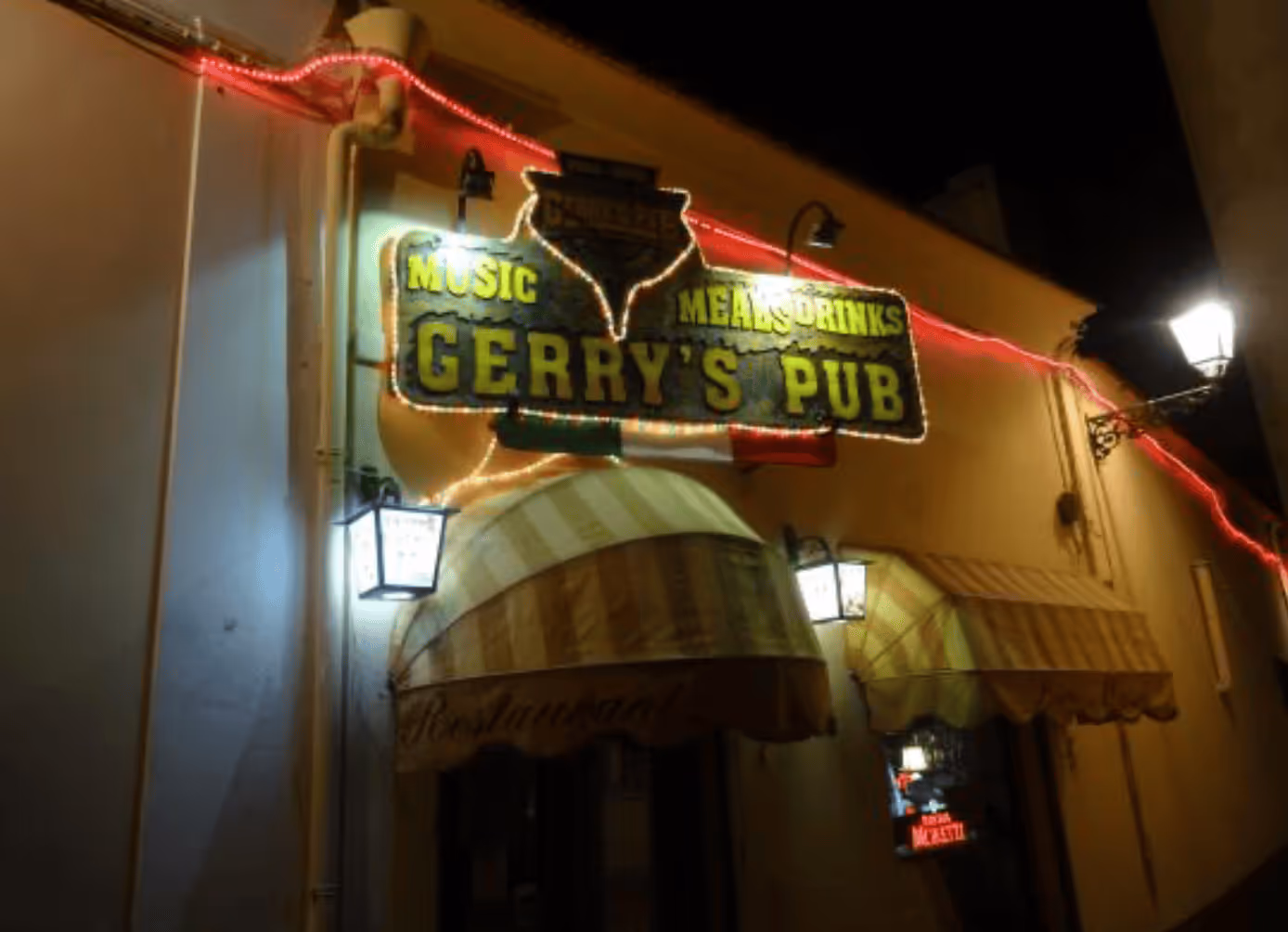 Illuminated sign for Gerry's Pub at night with yellow text reading Music, Meals, Drinks, and a small Irish flag below.