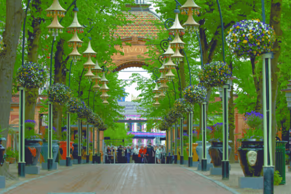 Pedestrian walkway lined with tall lamp posts adorned with hanging flower baskets, leading to a distant brick archway.