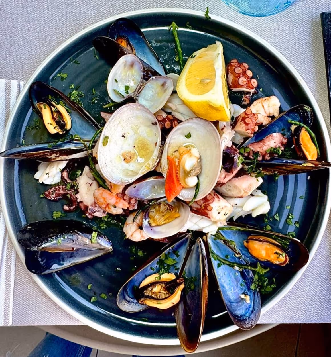 Plate of mixed seafood including mussels, clams, shrimp, and octopus garnished with herbs and a lemon wedge.
