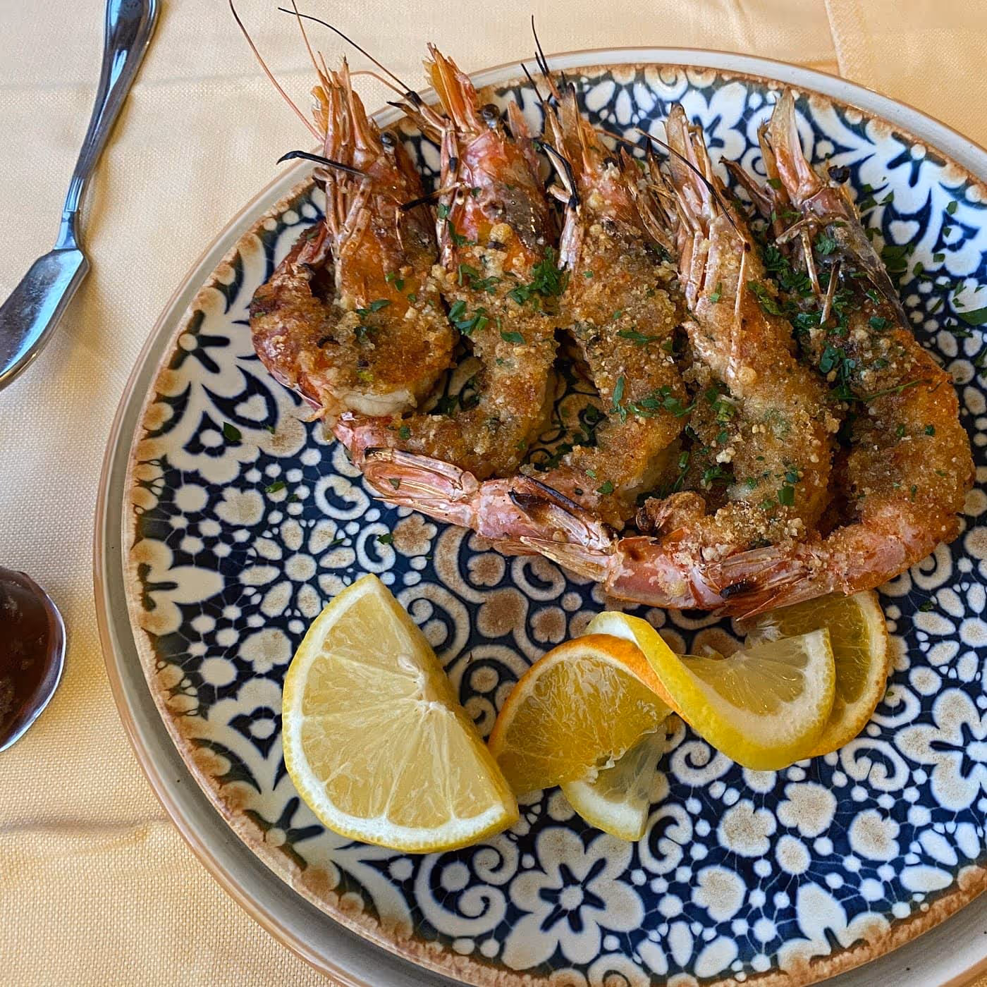Plate with grilled shrimp topped with garlic and herbs, accompanied by lemon and orange wedges on a decorative blue and white plate.