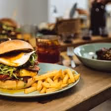 Cheeseburger with lettuce, tomato, and sauce served with French fries on a plate on a wooden table.