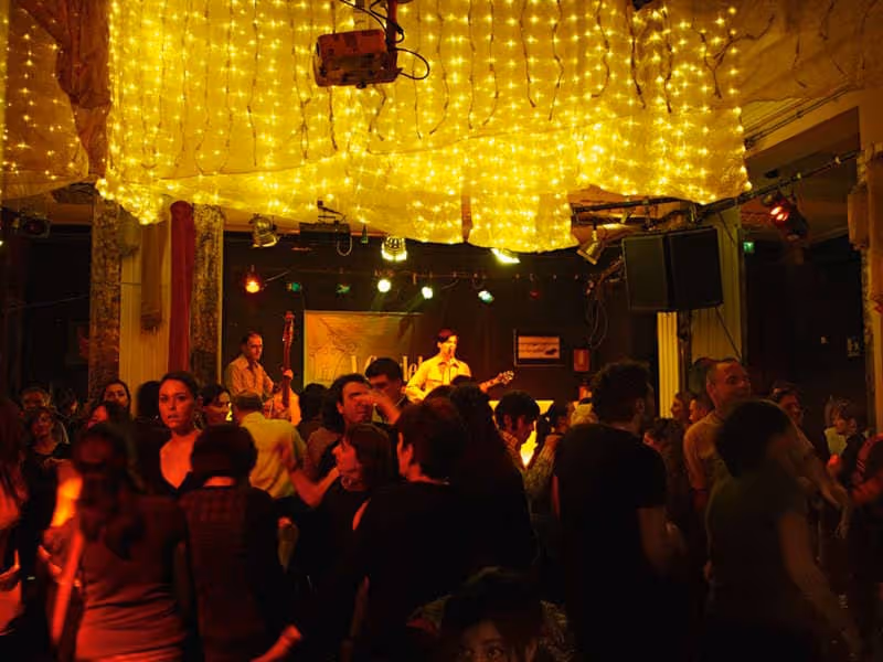Crowded indoor live music venue with string lights overhead and a band performing on stage.