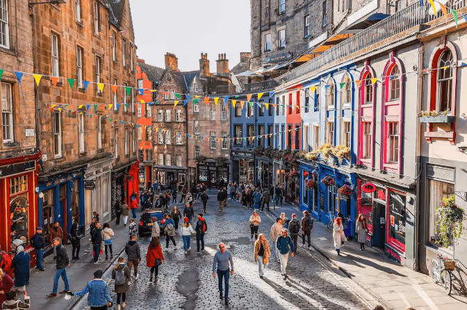 Crowded cobblestone street lined with colorful historic buildings and festive bunting overhead in a lively city setting.