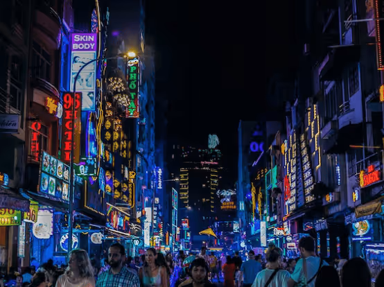 Bustling city street at night brightly lit with neon signs and crowds of people.