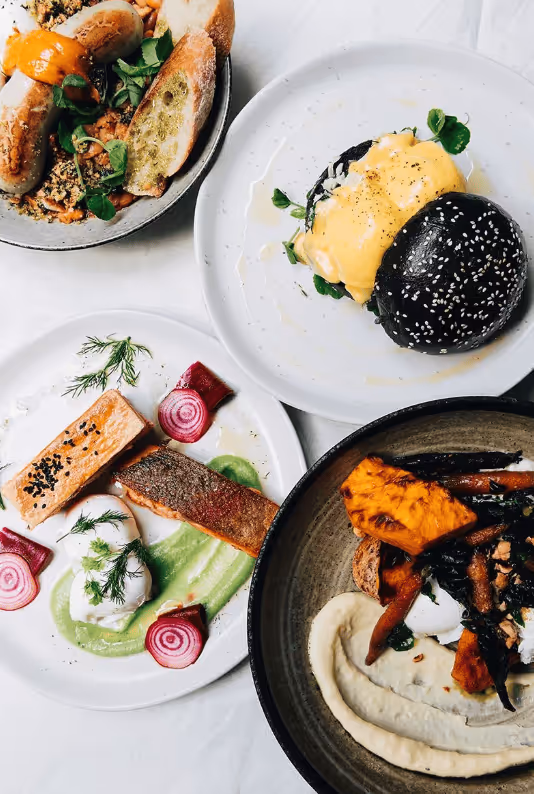 Four gourmet dishes including a black sesame bun sandwich, grilled salmon with beet slices and green sauce, roasted vegetables on creamy puree, and a bowl with bread slices and sauce.