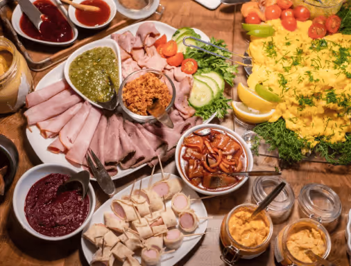 Assorted sliced meats, sauces, pickles, and eggs on a wooden table arranged for a meal.