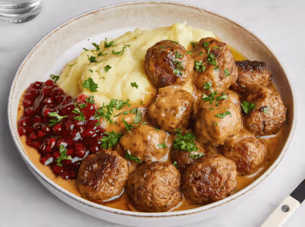 Plate with Swedish meatballs in gravy, mashed potatoes, and lingonberry sauce garnished with chopped parsley.