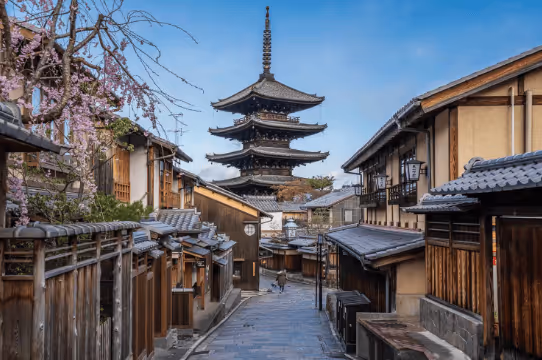 Traditional Japanese street with wooden houses leading to a tall five-story pagoda under a clear blue sky.