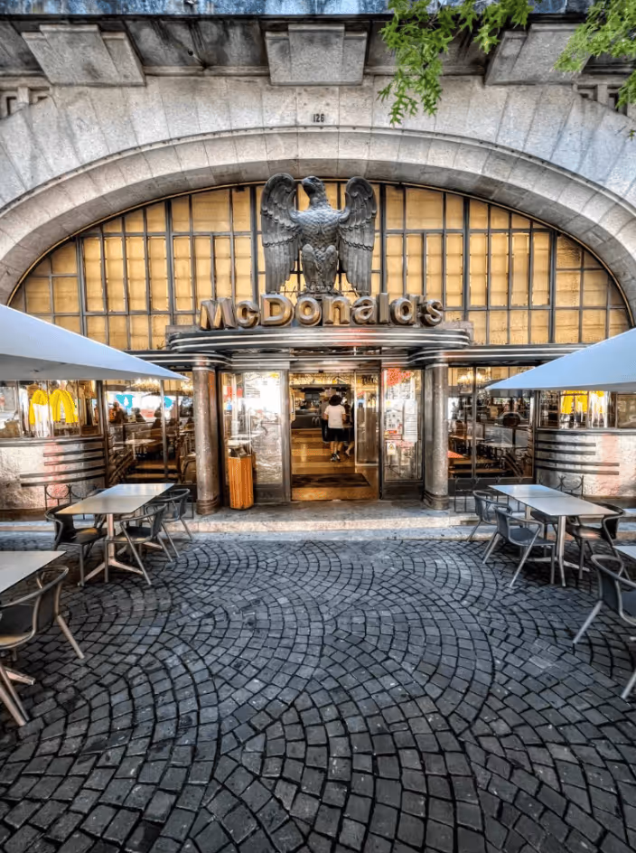 McDonald's restaurant with an outdoor seating area under white umbrellas and a large eagle sculpture above the entrance.
