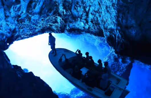 Group of people on a small boat inside a glowing blue cave.