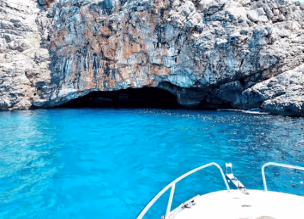 View from a boat approaching a rocky sea cave with bright turquoise water.