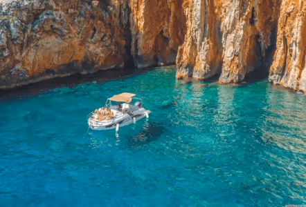 Small white boat floating on clear turquoise water near orange rocky cliffs.