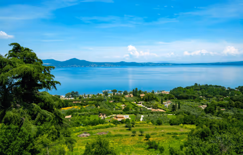 Scenic view of a large blue lake surrounded by green trees and fields under a partly cloudy sky.