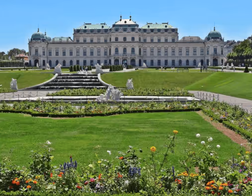 Baroque palace with green patinated roofs, manicured lawn, and flower beds under a clear blue sky.