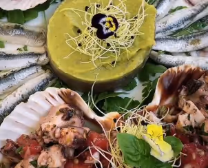 Plated seafood dish with marinated octopus in scallop shells, topped with greens and edible flowers, accompanied by a smooth green mousse with garnish.