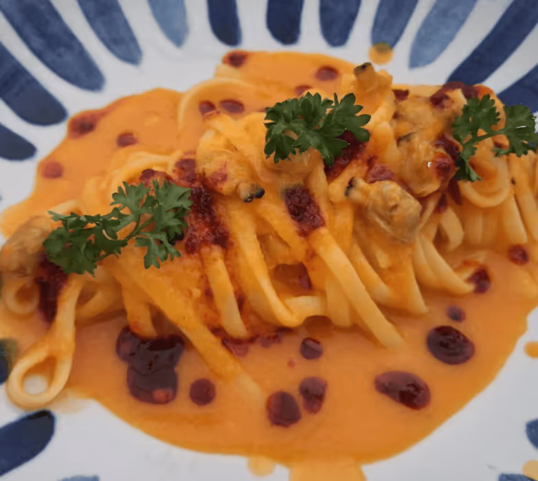 Plate of pasta with creamy orange sauce, garnished with parsley and drops of red chili oil.