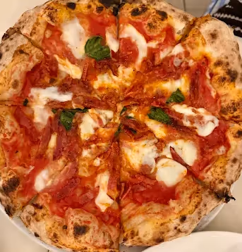 Neapolitan-style margherita pizza with tomato sauce, mozzarella, and basil leaves on a white plate.