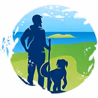 Silhouette of a person holding a walking stick standing next to a dog, with a scenic background of blue sky, green grass, and distant hills.