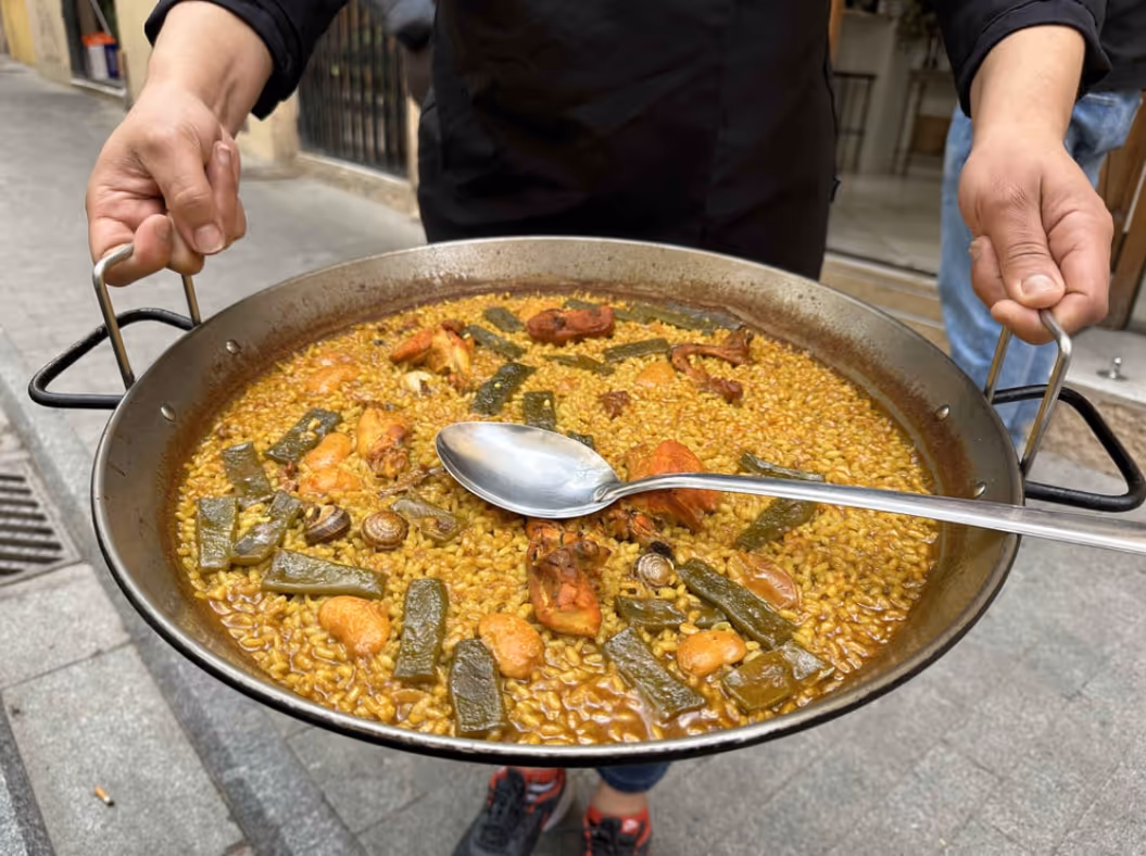 Person holding a large pan of traditional Valencian paella with rice, green beans, snails, and chicken pieces.