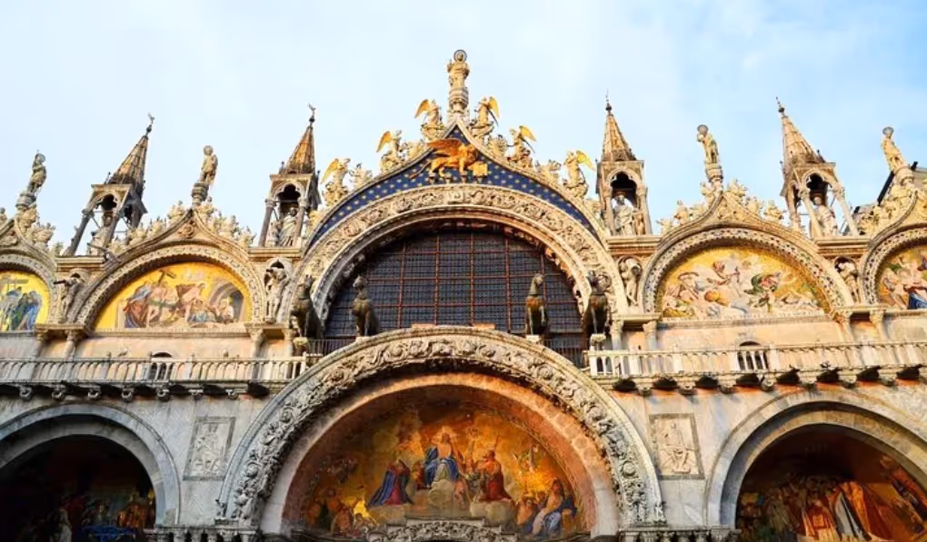 Facade of St. Mark's Basilica in Venice featuring ornate arches, detailed mosaics, and golden statues.