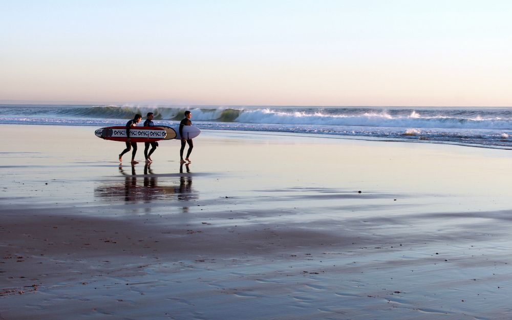 three people with boards going out to surf