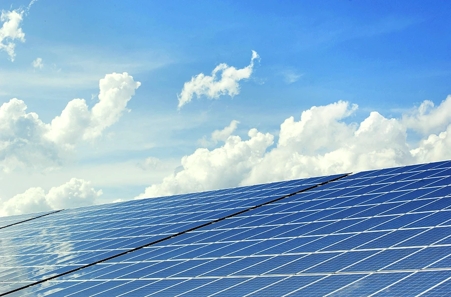 Campo di pannelli fotovoltaici sotto un cielo azzurro con nuvole bianche, rappresentazione di produzione di energia solare.