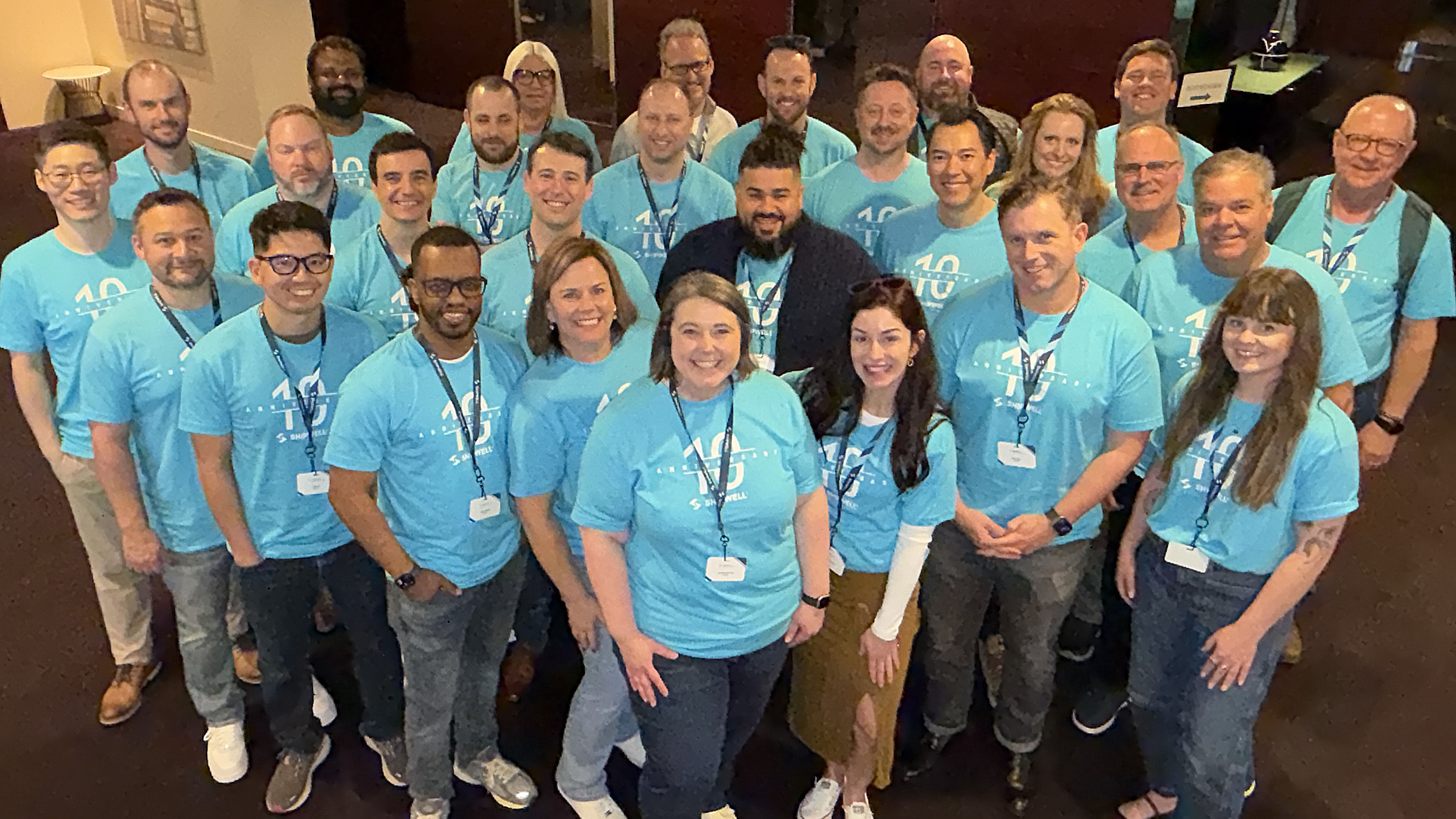 Large group of Shipwell employees in light blue t-shirts with Shipwell 10 Year Anniversary logo on them.