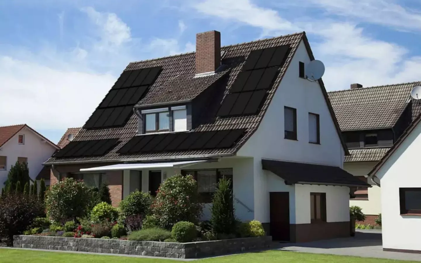 Residential house with brown tiled roof equipped with multiple black solar panels and a well-maintained front garden.
