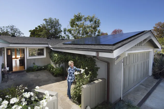 Una signora sta sistemando il giardino di una casa con un impianto fotovoltaico SunPower