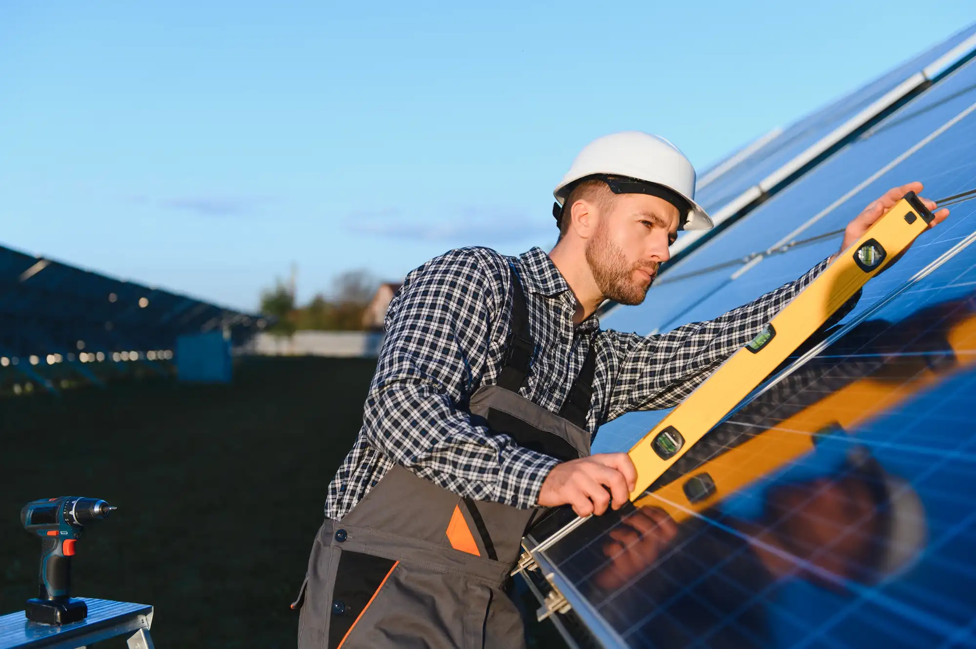 Technician wearing a hard hat using a level tool to check alignment of solar panels outdoors.