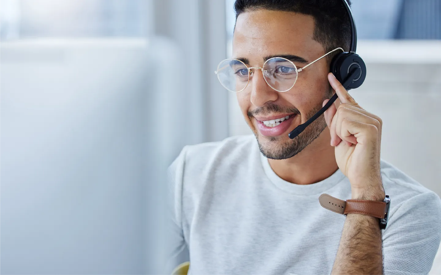 Smiling man wearing glasses and headset with microphone using a computer.
