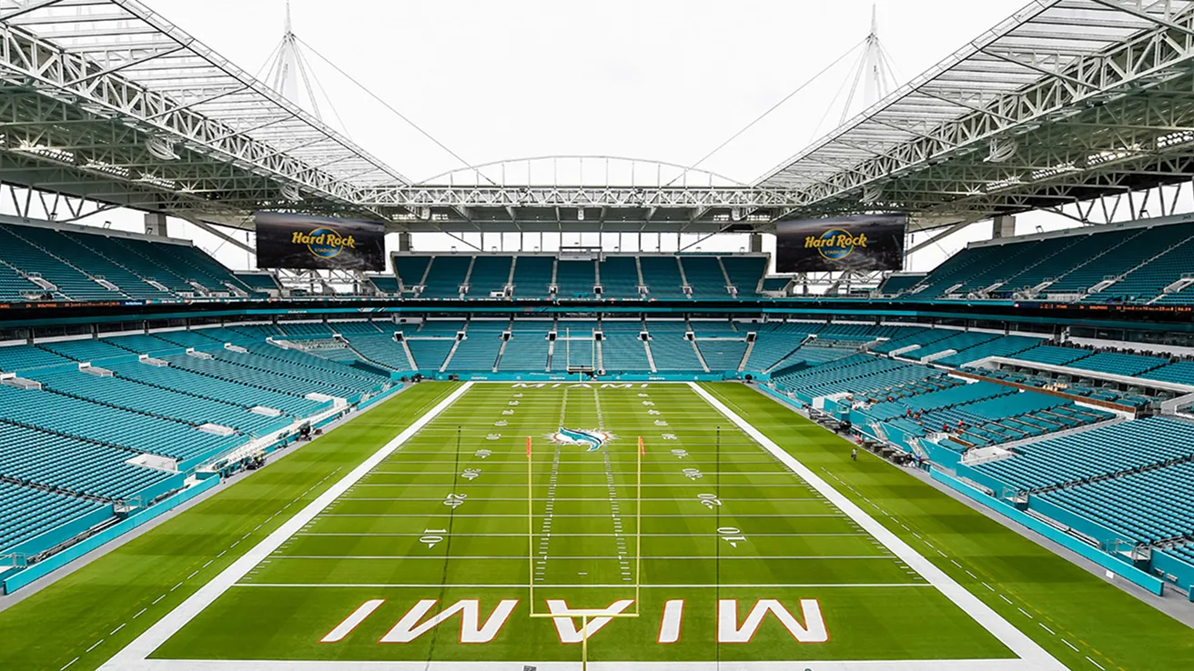 Hard Rock Stadium in Miami, home of the Miami Dolphins, showcasing empty teal seating and a professionally maintained NFL football field under retractable roof structure