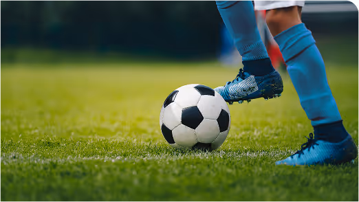 Close-up of soccer player in blue cleats dribbling black and white ball on a well-maintained green field during daytime