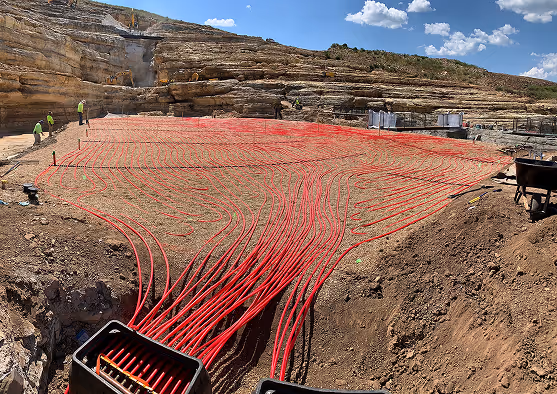 Close-up image of active hydronic tubing system installed in an excavation site, showing vibrant red piping for subsurface turf management.