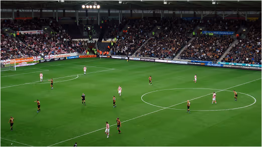 Soccer players mid-game on a green stadium field with fans in the stands, illustrating in-game turf durability under high-performance play