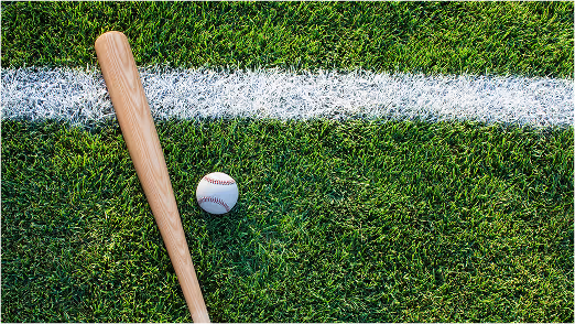 Close-up of a wooden baseball bat and ball lying on green turf next to a white chalk baseline