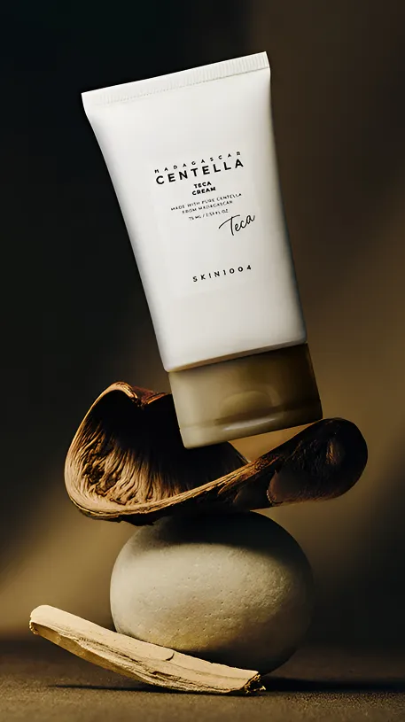 Tube of Madagascar Centella Teca Cream balancing on natural stones and a shell in warm light.