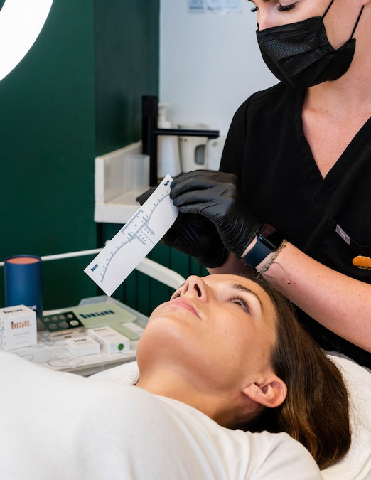 	Artist measuring brow shape with a mapping ruler before microblading