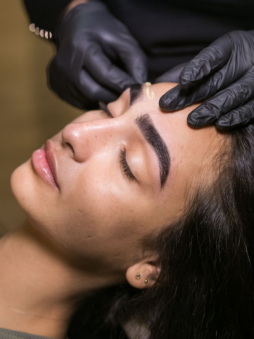 Artist checking brow shape and density on a reclined client