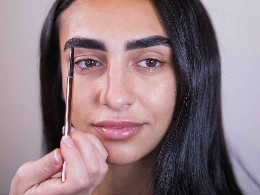 Brow pencil held upright to map where the brow should start