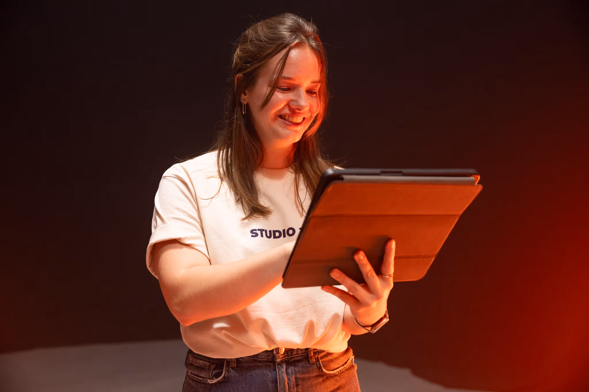 Vrouw lacht terwijl ze een tablet gebruikt, in een warme, rood verlichte omgeving.