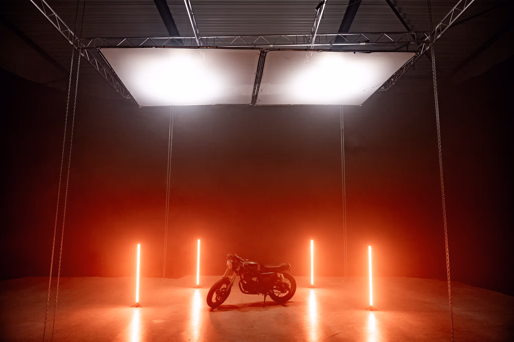 Motorfiets in een donkere studio met vier verticale oranje neonlichten en twee grote verlichtingspanelen aan het plafond.