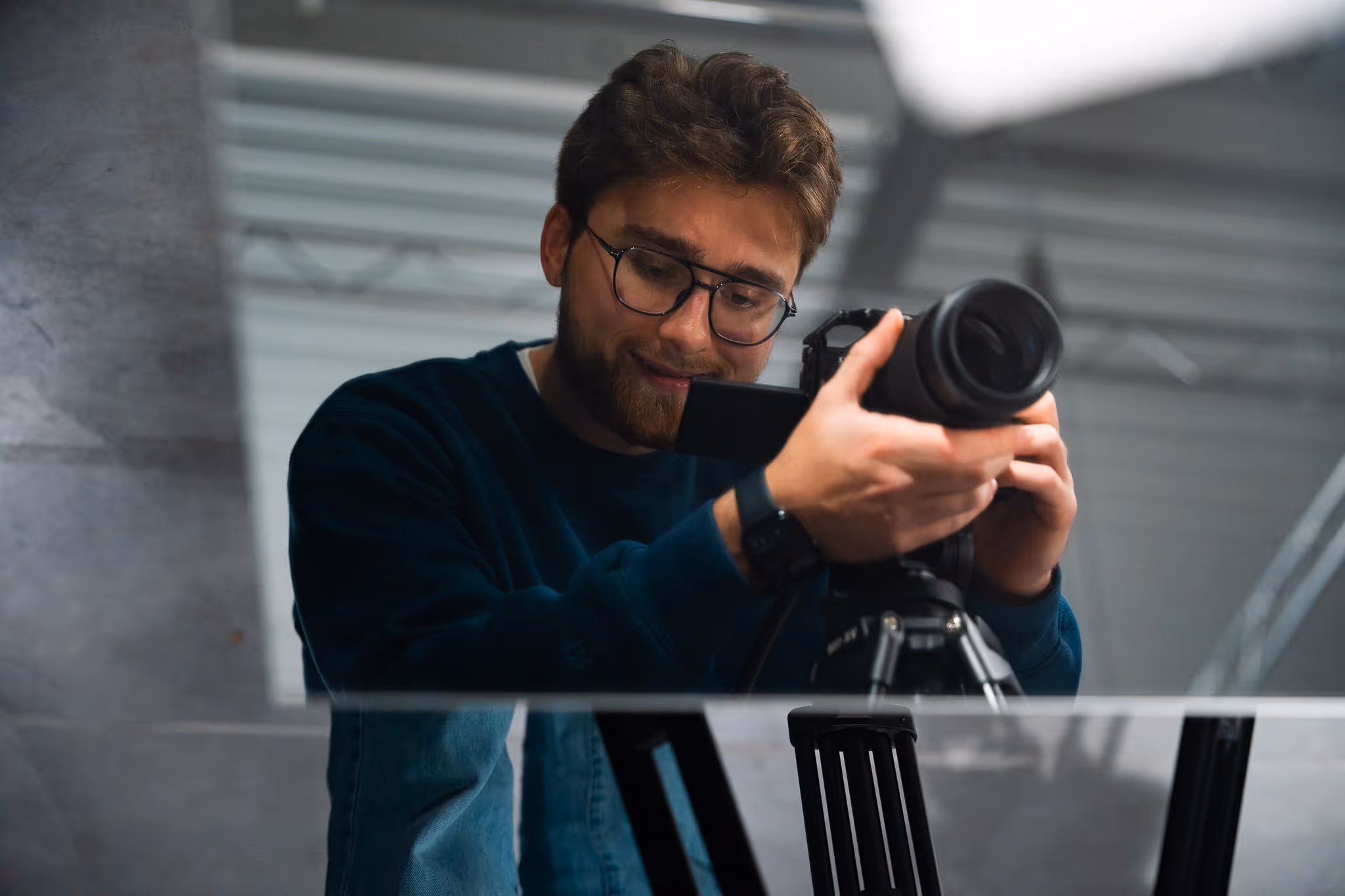 Man met bril en baard die een camera op een statief instelt in een binnenruimte.